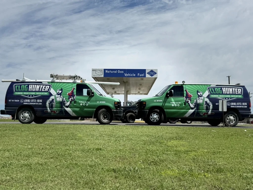 Two wrapped Clog Hunter plumbing vans fueling at a natural gas station near Tahlequah, Oklahoma