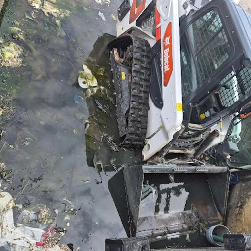Clog Hunter running a skid steer to clear a flooded excavation